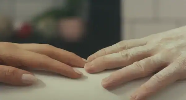Close-up of two hands gently touching on a table. One hand is older and more wrinkled, while the other is younger.