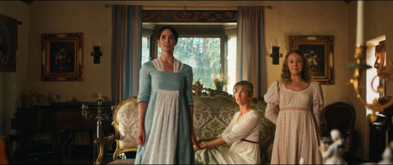 Three women in regency-era dresses stand and sit in an elegant living room with vintage furniture and framed art, conveying a period drama atmosphere.