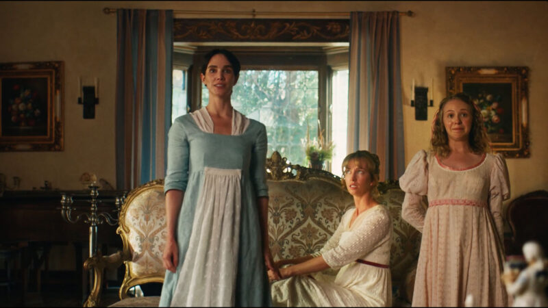 Three women in regency-era dresses stand and sit in an elegant living room with vintage furniture and framed art, conveying a period drama atmosphere.