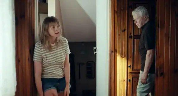 A young girl with long hair and striped shirt talking to an older man with short gray hair at a doorway in a home interior.
