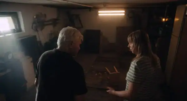 Two people having a conversation in a dimly lit room with warm lighting, surrounded by various objects and furniture.