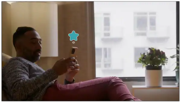 Person relaxing on a sofa using a smartphone near a window with a potted plant, capturing a cozy indoor scene for lifestyle and technology themes.