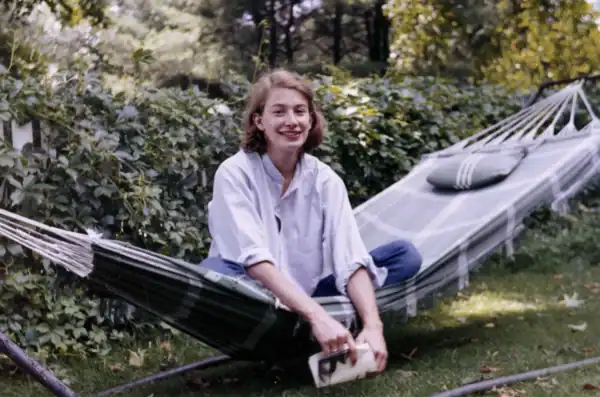Young woman relaxing on a hammock in a lush garden, smiling and enjoying nature in a peaceful outdoor setting.