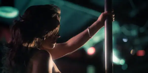 Person holding a pole in a dimly lit environment with colorful lights, possibly at a nightclub or dance event.