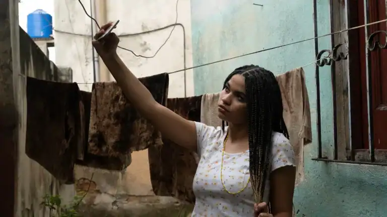 Young woman with braided hair taking a selfie outdoors near laundry hanging on a clothesline in an urban setting.