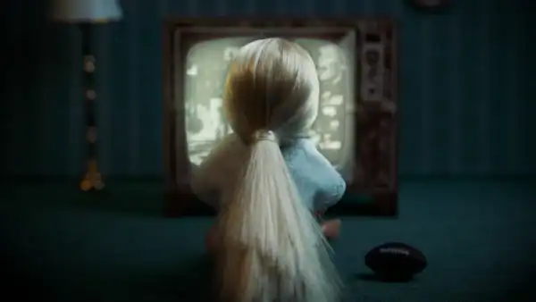 A doll watching a vintage television screen in a dimly lit room, with a remote control nearby.