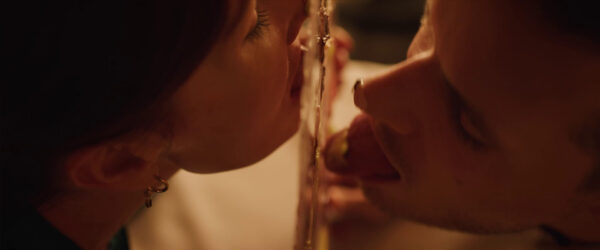 Two people are licking opposite sides of a glass pane, focusing on connection.