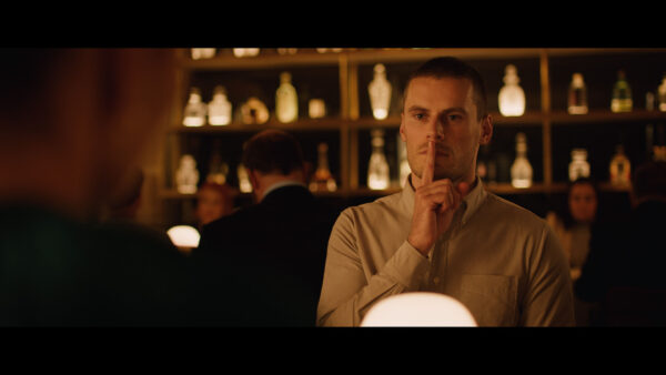 A man in a bar gestures "shh" with his finger to his lips.