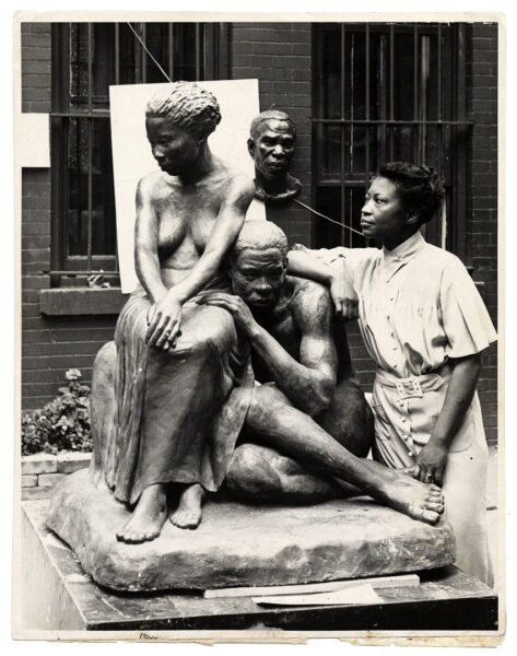 Black and white photo of artist Augusta Savage beside her sculpture Realization (1936), showing two seated figures in a contemplative pose.