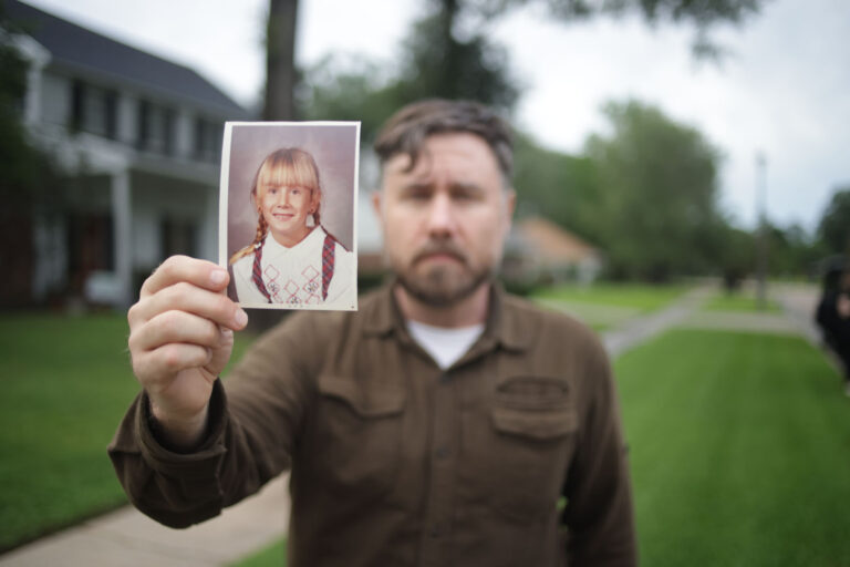 A man, facing the camera, holding a photo of a little girl.