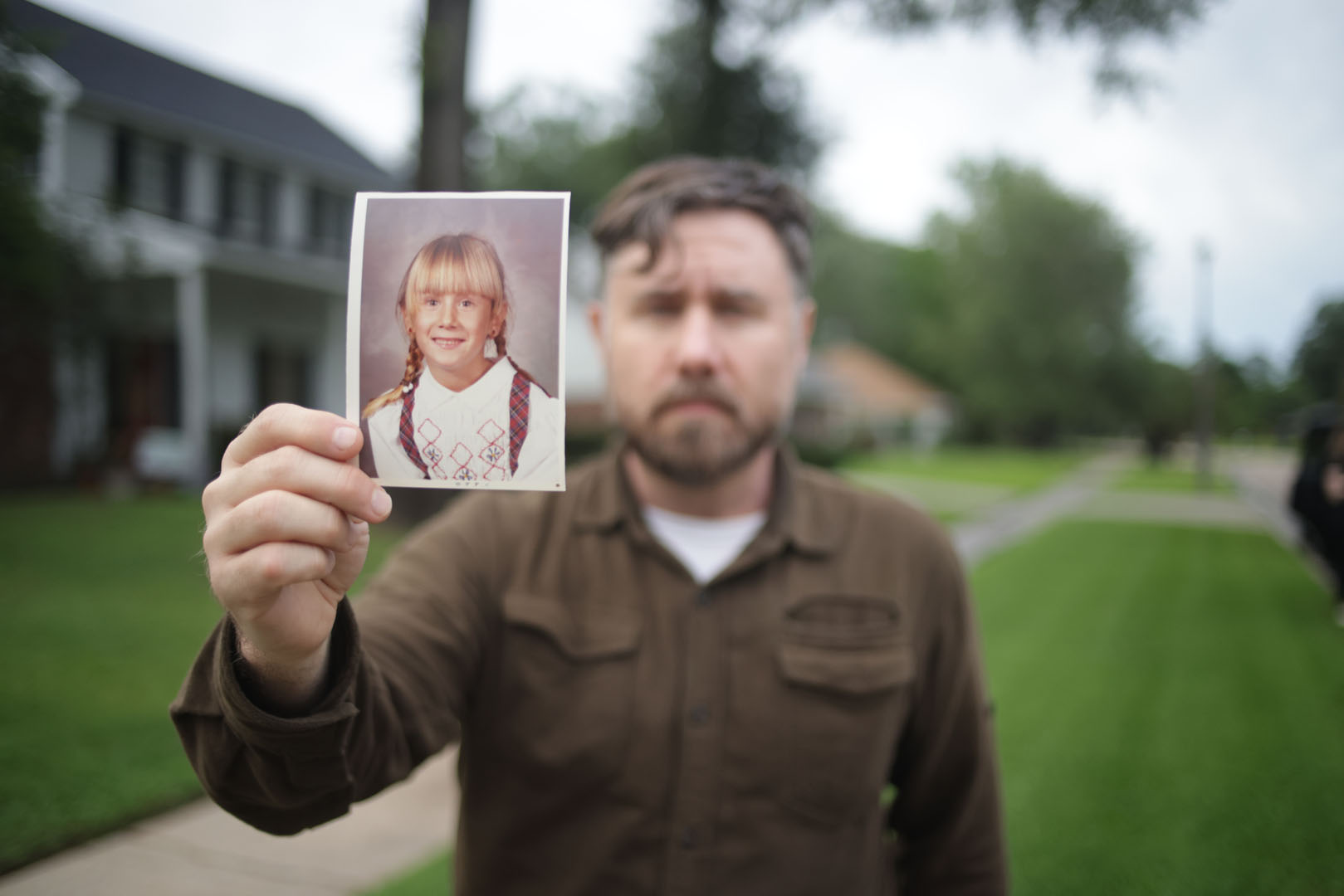A man, facing the camera, holding a photo of a little girl.