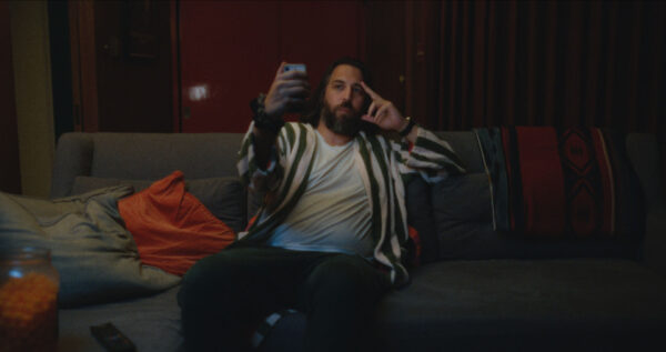 a man sitting on a couch, taking a selfie.