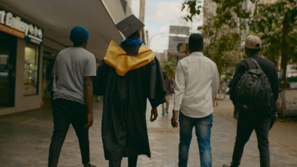 Four people walk down a city street. One wears a graduation cap and gown, conveying achievement.