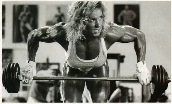 A muscular woman bends over while lifting a dumbbell.