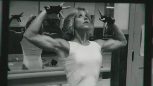 A woman wearing fingerless gloves looks up to the sky while flexing her arms.