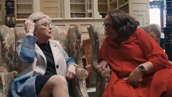 Two older women sit in armchairs in discussion with each other.