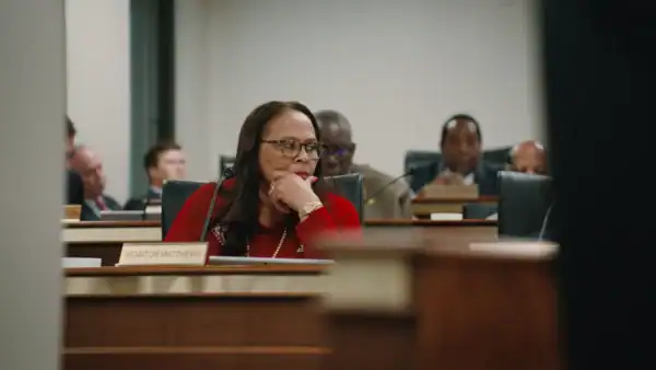 A woman in a court-like setting .looks off to the right with a contemplative look on her face.