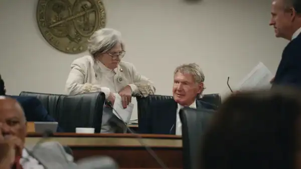 A woman stands while talking to a man in a suit sitting a a desk.