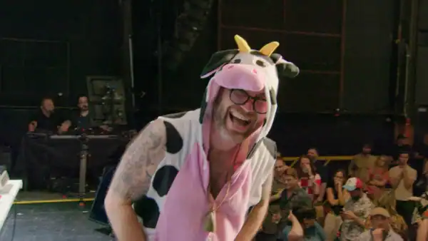 A man in a cow onesie laughs and bends over.