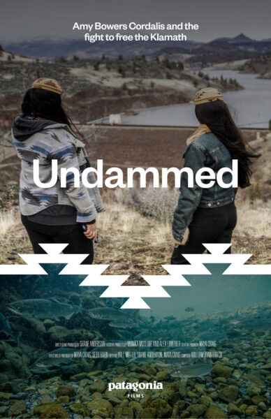 Film poster for Undammed. At the top, text reads: “Amy Bowers Cordalis and the fight to free the Klamath.” The title Undammed appears in bold white letters across the center. Two women stand with their backs to the camera, looking out over a river and mountainous landscape. Below, a graphic zigzag pattern separates the upper landscape image from an underwater scene of fish swimming among rocks. At the bottom, production credits are listed along with the Patagonia Films logo.
