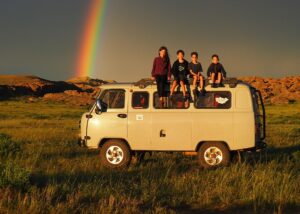 4 children sitting on the roof of a van with red rocks and a rainbow in the background