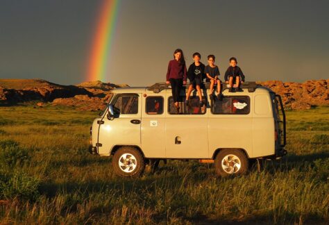 4 children sitting on the roof of a van with red rocks and a rainbow in the background