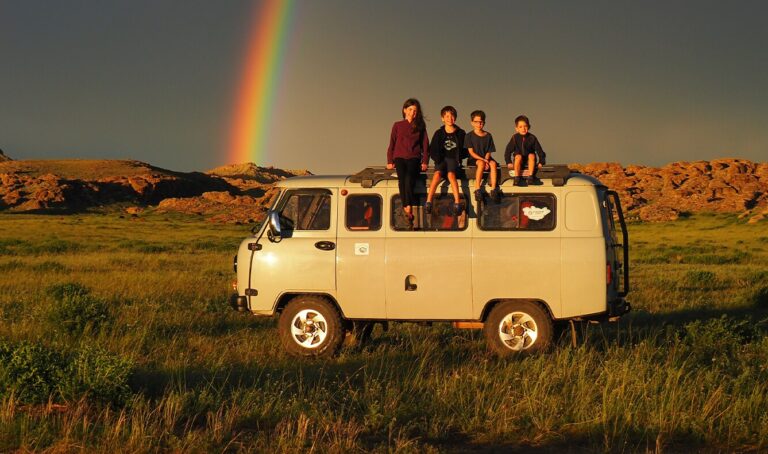 4 children sitting on the roof of a van with red rocks and a rainbow in the background