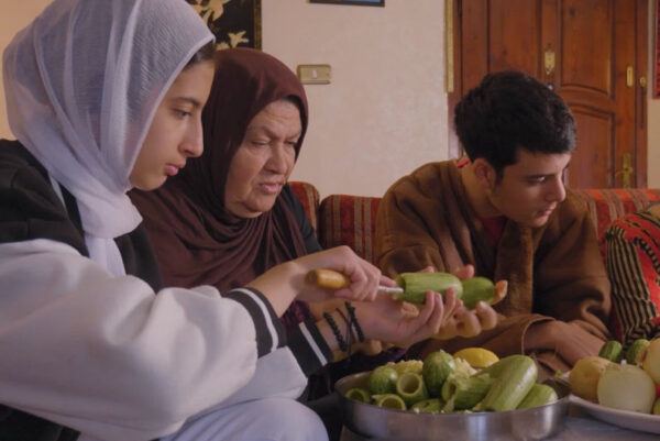 Three people sit together coring vegetables in a living room, with a large bowl of vegetables on the table in front of them.