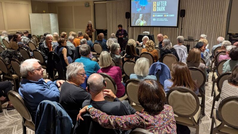 Audience in an event room waiting for a film event to begin, with "SAT AFTER DARK" and film options projected on a large screen at the front of the room.
