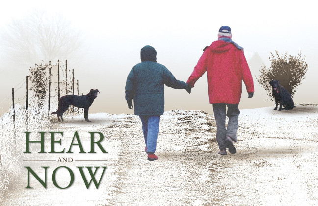 Hear and Now: a couple holding hands while walking down a snowy road with a black dog