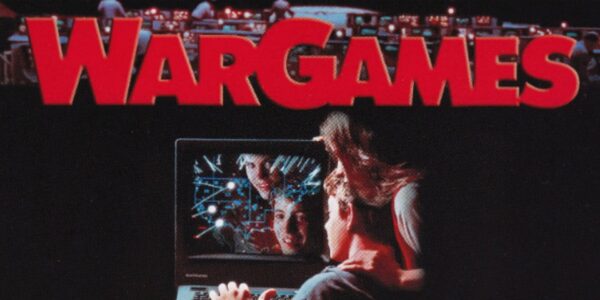 The title "WARGAMES" in large red letters above a computer screen showing a game with multiple faces reflected on it, with people looking at the screen.