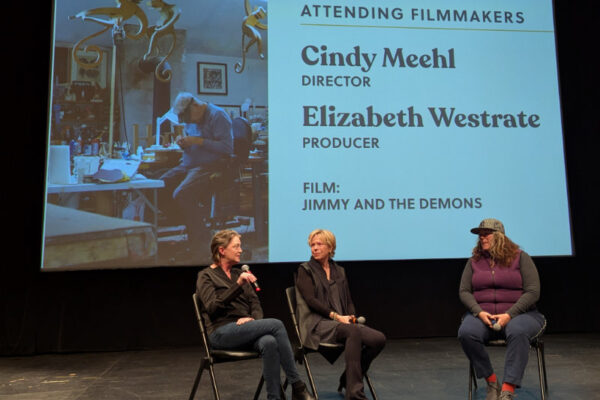 Three women sit on stage in front of a screen listing Cindy Meehl and Elizabeth Westrate as attending filmmakers for the film "Jimmy and the Demons.
