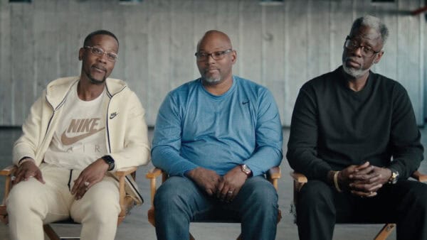 Three men sitting in chairs against a concrete wall, engaged in a serious discussion, representing a witness recanting in a legal or testimonial context.