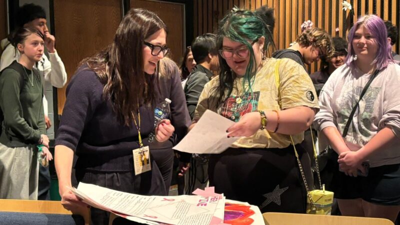 A filmmaker stands and talks with a student at the RMWF Youth Outreach program.